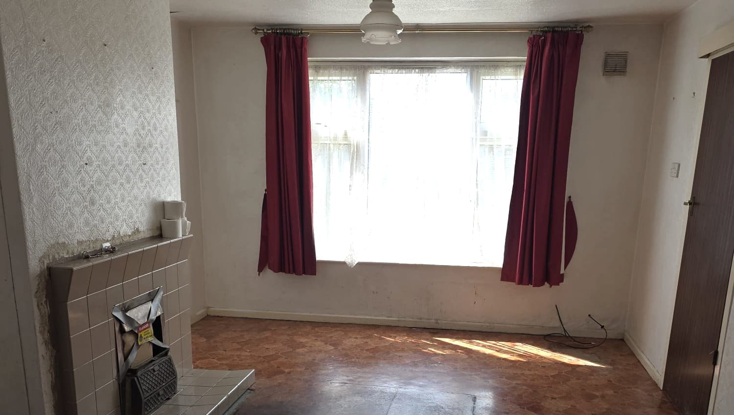 A cleared living room with red curtains at the window and sunlight on the floor