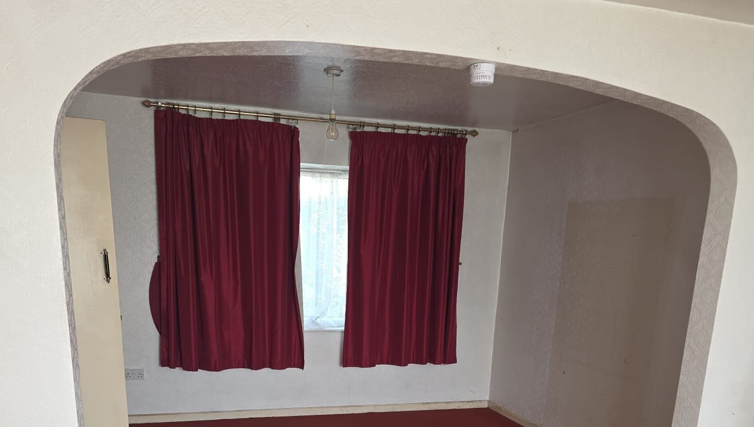 An empty room seen through an archway, with red curtains and red carpet