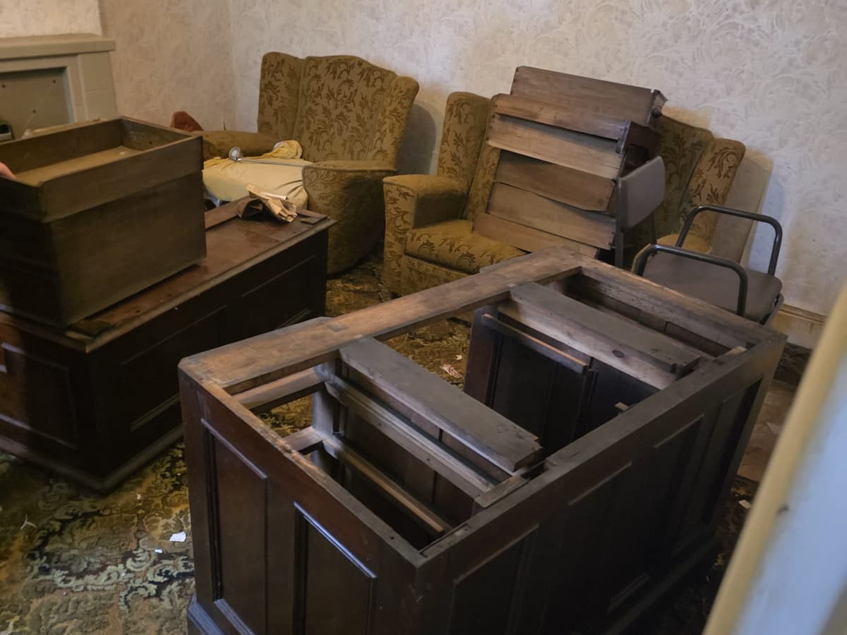 Dark wood furniture and two armchairs gathered in a front room during a clearance