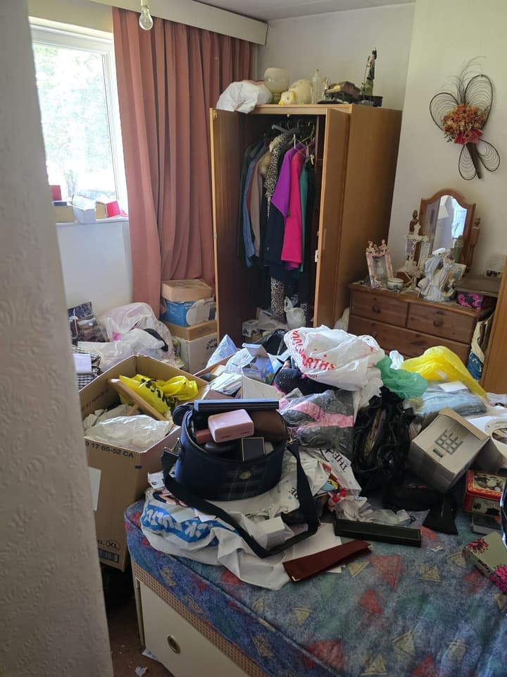 Bedroom before the clearance: a wardrobe, a dressing table and a bed covered in bags and boxes