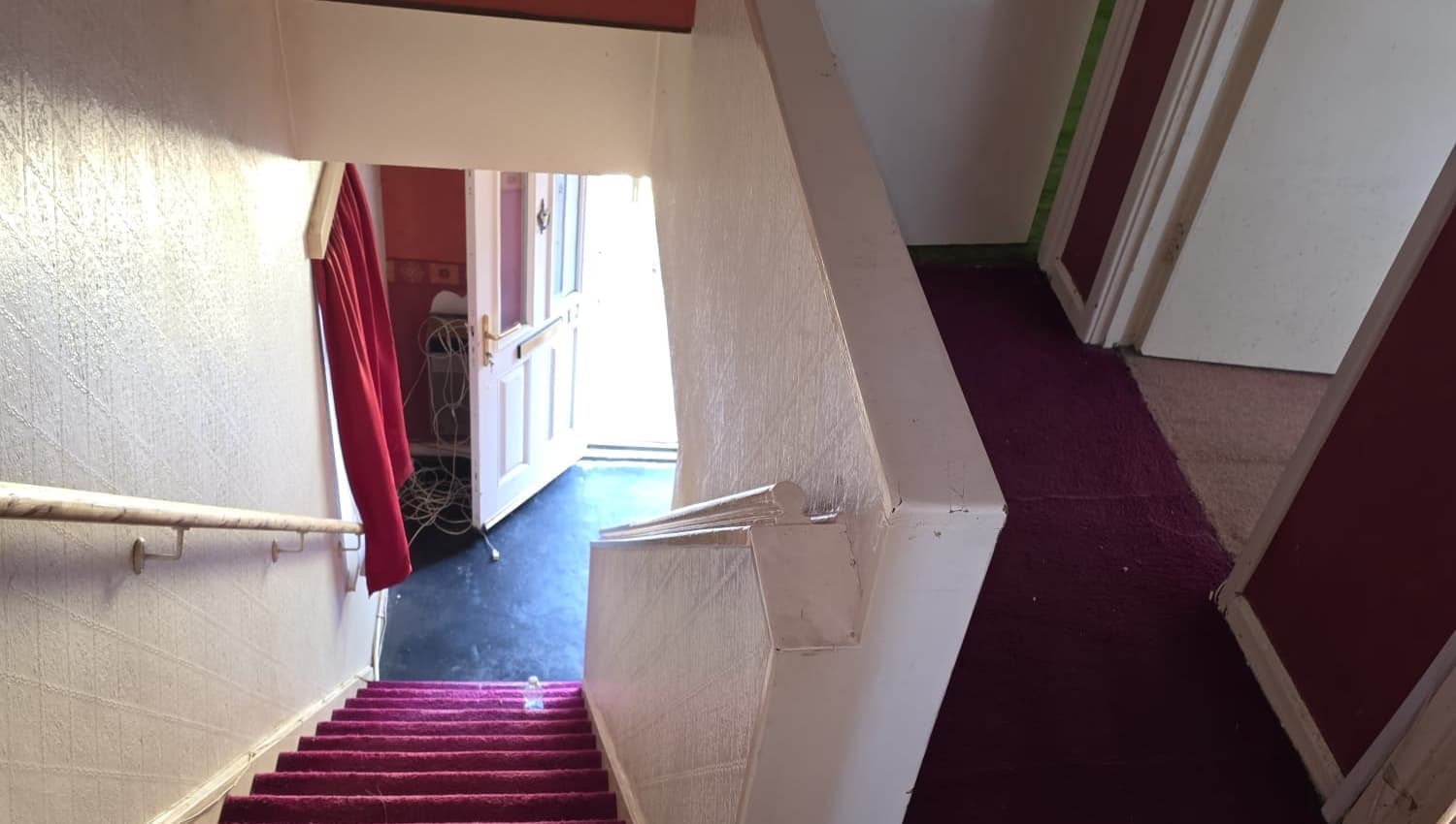 A cleared staircase and hall with red carpet, looking down to the front door